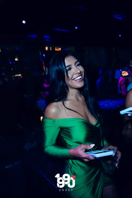 Smiling woman in a green dress, enjoying a nighttime party organized by 1990 Group in New York.