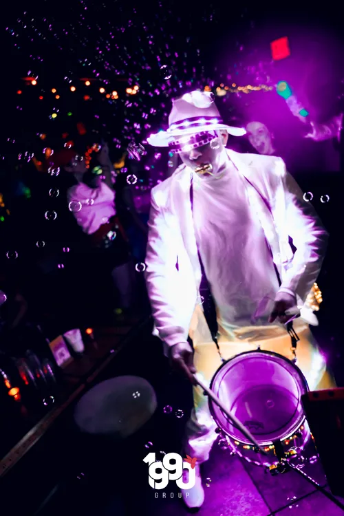 Artist in an illuminated suit playing a drum at a vibrant party by 1990 Group in New York.