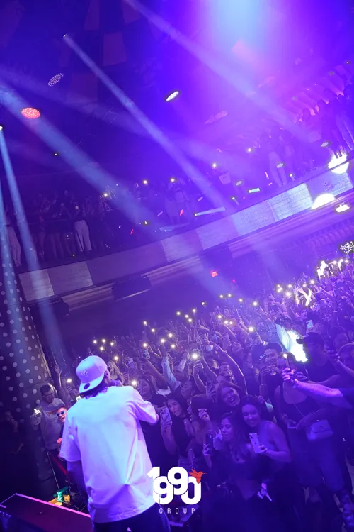 Artist Peso Pluma in the middle of a live show at a New York club, illuminated by purple lights, during an event organized by 1990 Group.