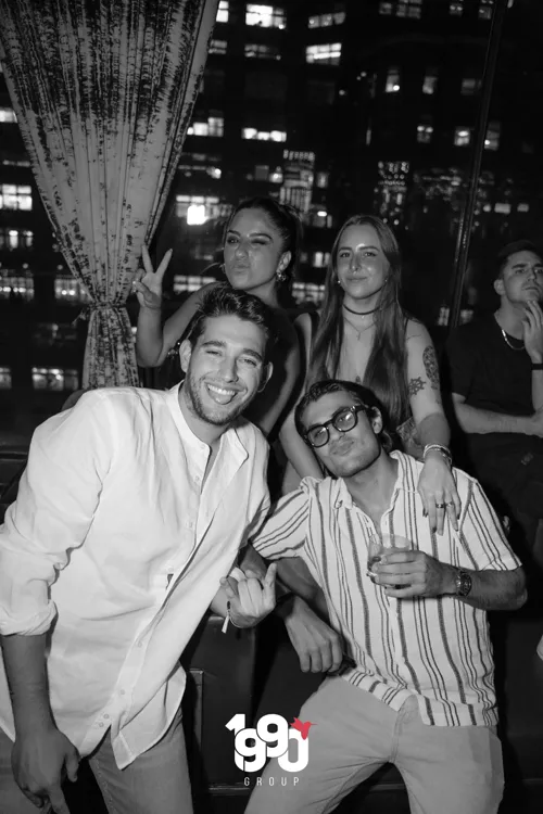 Group of friends having fun at a party in New York organized by 1990 Group, with the city skyline in the background.