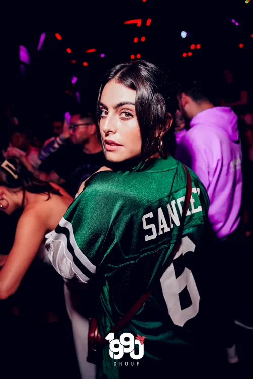 Woman posing from behind wearing a football jersey at a party organized by 1990 Group in New York.