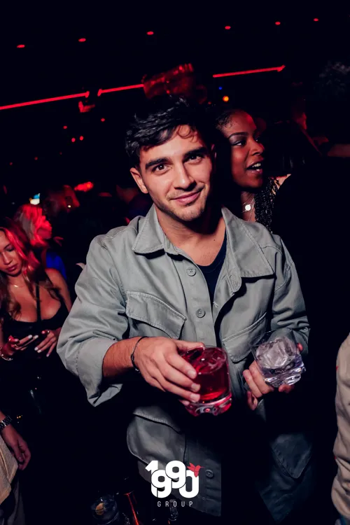 Young man holding a drink at a party organized by 1990 Group on a rooftop in New York.