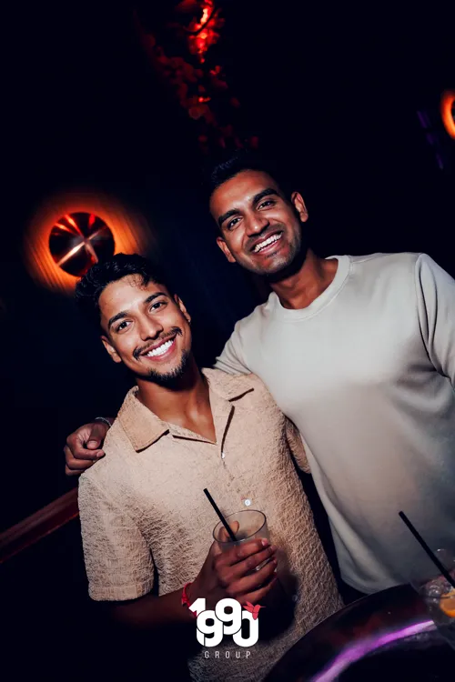 Two friends posing for a photo at a nighttime event in New York, organized by 1990 Group.